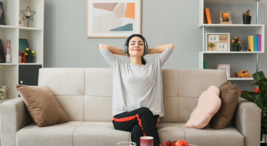 pleased-with-closed-eyes-with-hands-head-young-girl-wearing-headphones-sitting-sofa-coffee-table-living-room