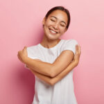 care-tenderness-concept-mirthful-positive-brunette-asian-female-hugs-herself-gently-tilts-head-smiles-happily-keeps-eyes-shut-from-pleasure-has-romantic-mood-dressed-casual-outfit