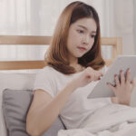 young-asian-woman-using-tablet-while-lying-bed-after-wake-up-morning