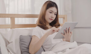 young-asian-woman-using-tablet-while-lying-bed-after-wake-up-morning
