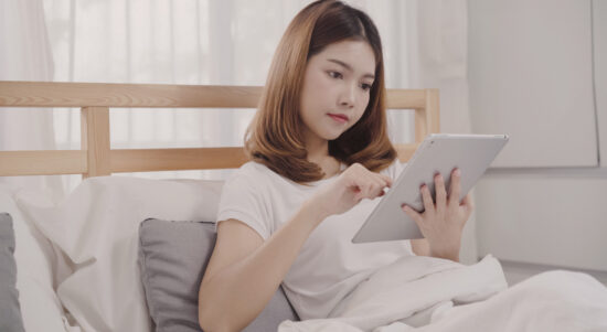young-asian-woman-using-tablet-while-lying-bed-after-wake-up-morning