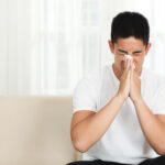 young-asian-man-sitting-couch-home-blowing-nose-with-tissue