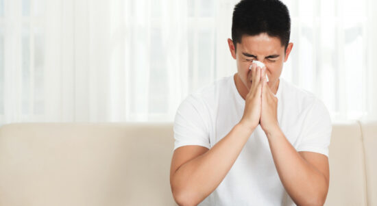 young-asian-man-sitting-couch-home-blowing-nose-with-tissue