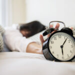sleepy-woman-reaching-holding-alarm-clock